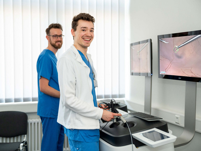 Zwei Studierende in blauer OP-Kleidung stehen an einem digitalen Laparoskopie-Simulator an den Kreiskliniken Herford. 