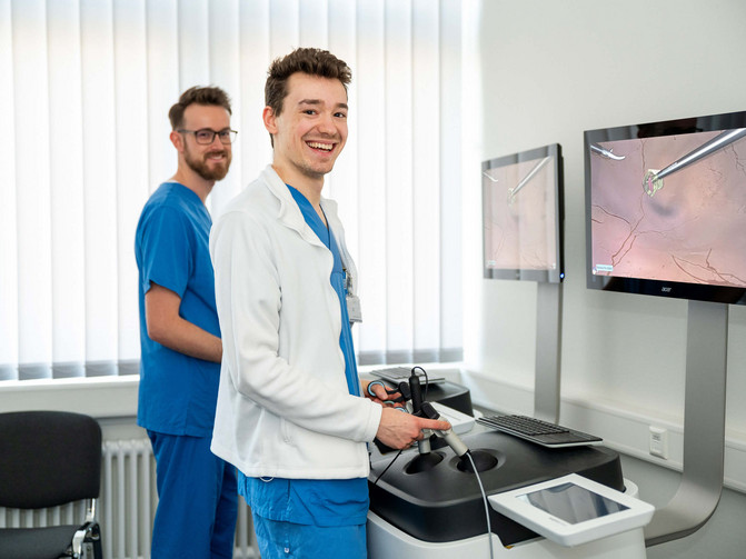 Two medical students in blue surgical scrubs stand at a digital laparoscopy simulator at the Herford Clinics.