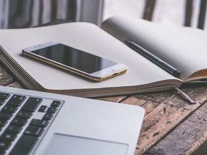 Laptop, Smartphone und Buch liegen auf einem Tisch