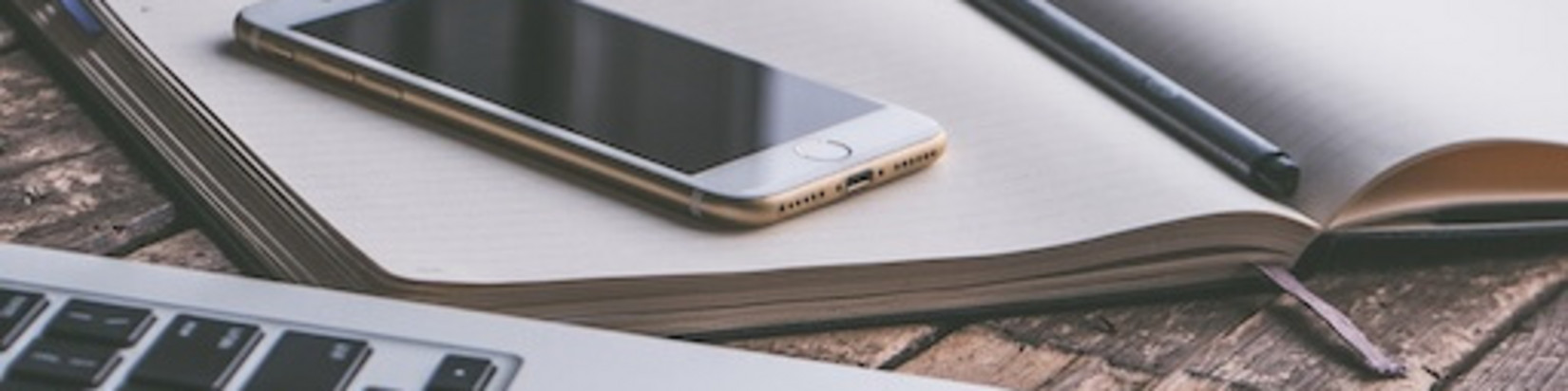 Laptop, Smartphone und Buch liegen auf einem Tisch