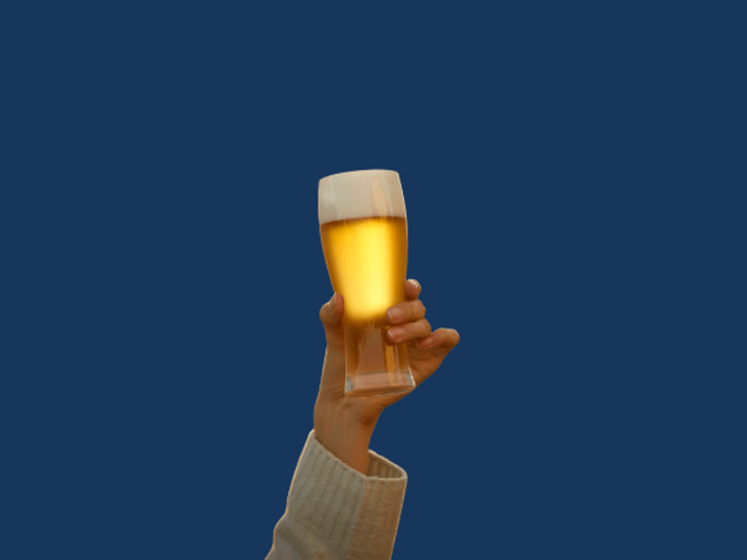 Auf dem Bild ist im Vordergrund eine Hand zu sehen, die ein volles Bierglas in die Luft hebt. Der Hintergrund ist RUB-Blau. 