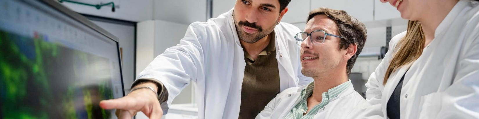 Drei Personen schauen auf einen Bildschrirm